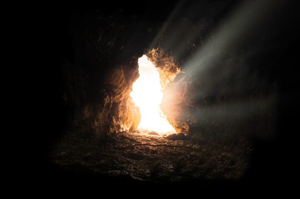 Warm sunlight breaking through a dark cave opening at sundown, symbolizing hope after darkness